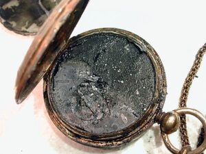 Photo of a Civil War era pocket watch caked with black mud.