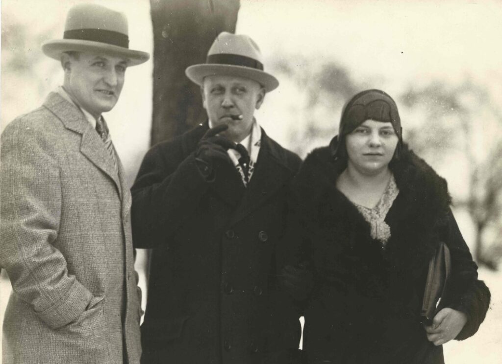 Two men and a woman standing outside wearing hats and overcoats.